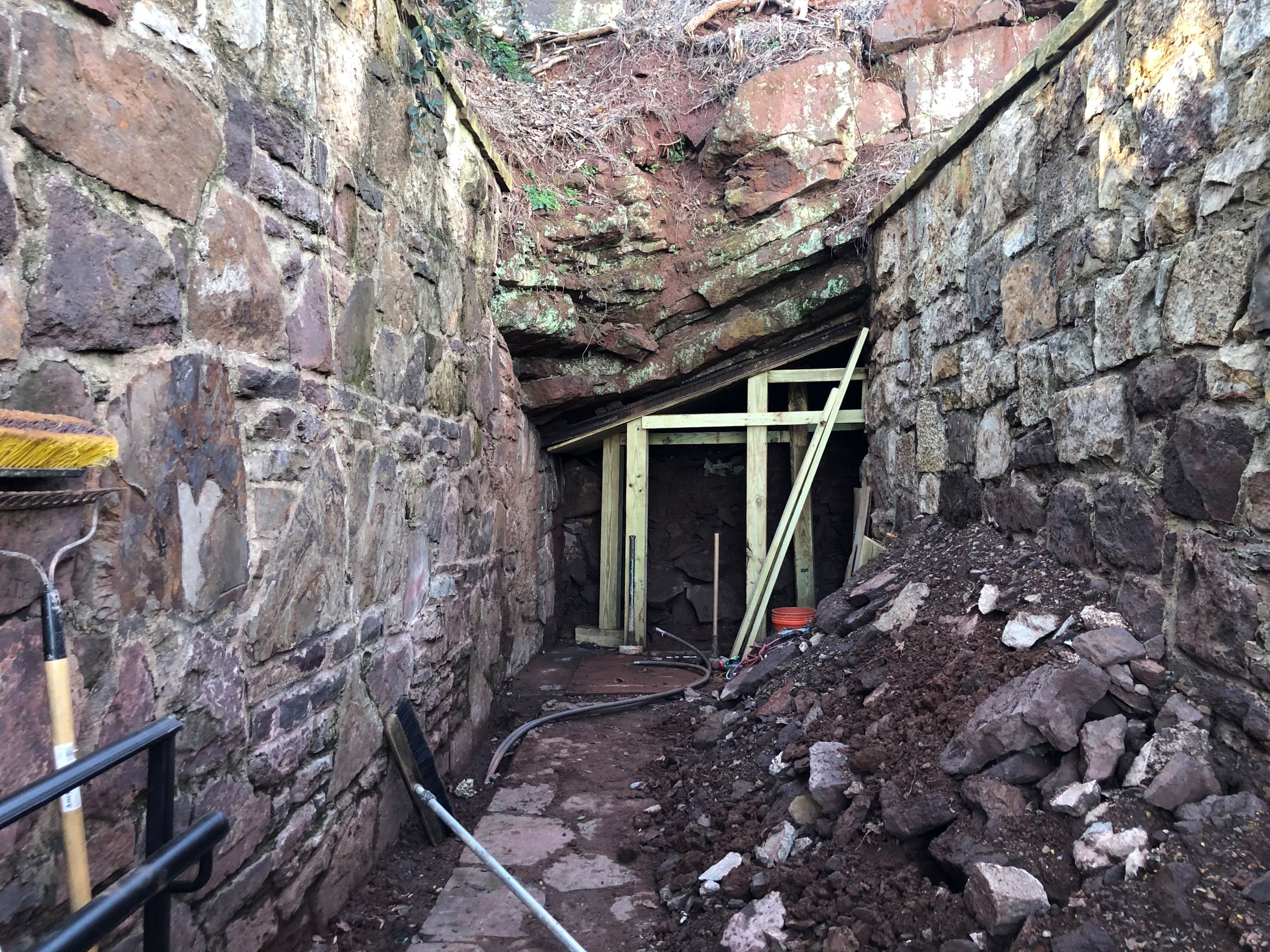 Entrance to mine after demolition of bricks covering opening. Dirt and rocks are piled up on the right side against rock wall. 
