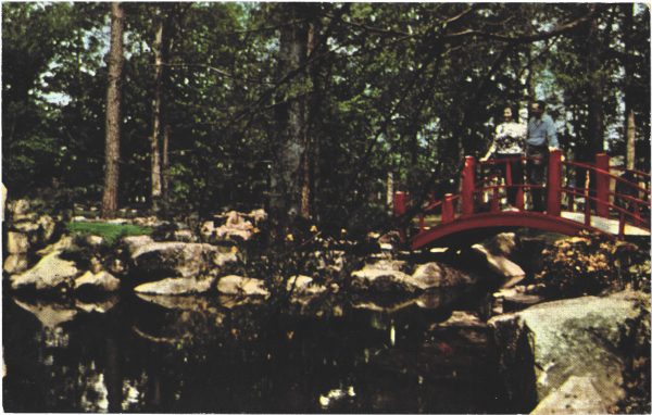 A small lake surrounded by large brown rocks with s small red bridge to the right